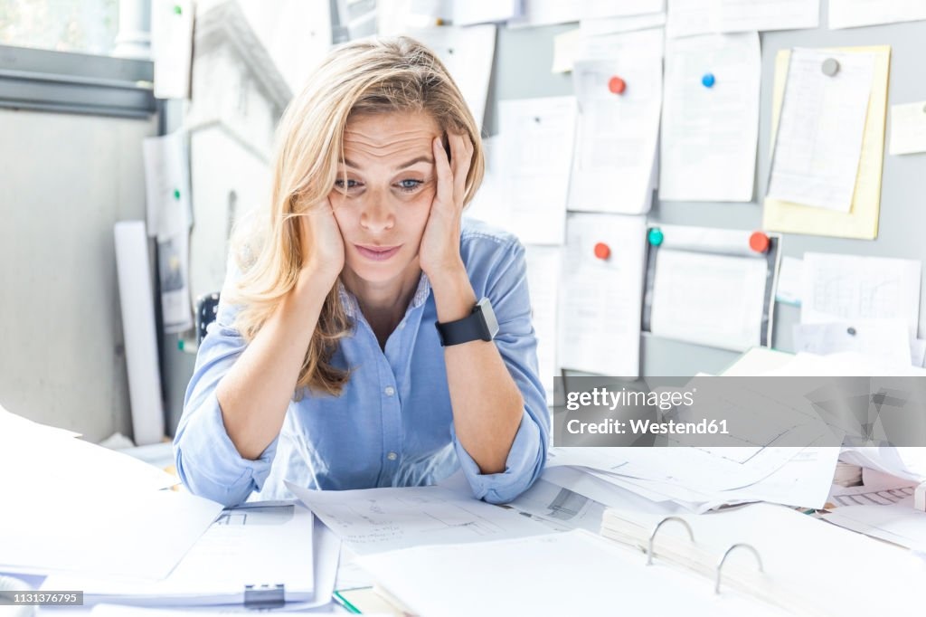 stressed person at desk, surrounded by papers