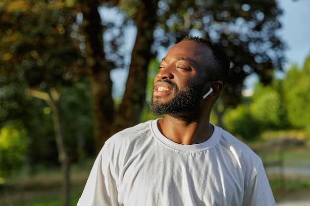 person wearing open-ear headphones, smiling, walking in park